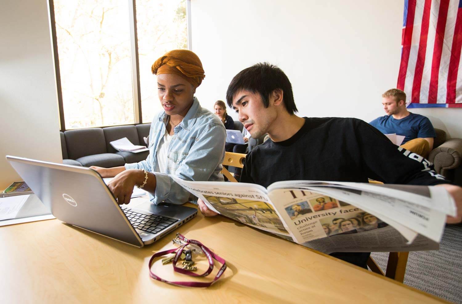 Students looking at laptop and newspaper