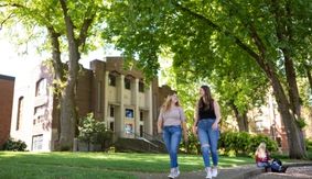 Two SPU students walk and talk in Tiffany Loop, with McKinley Hall in the background.