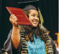 A new graduate holding up her diploma at Commencement