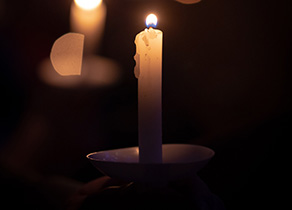 A candle lit against a dark background, with other candles out of focus, photo by Tim Umphreys