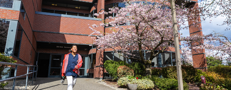 A female business student exits McKenna Hall on a spring day, with a cherry tree blooming to her left