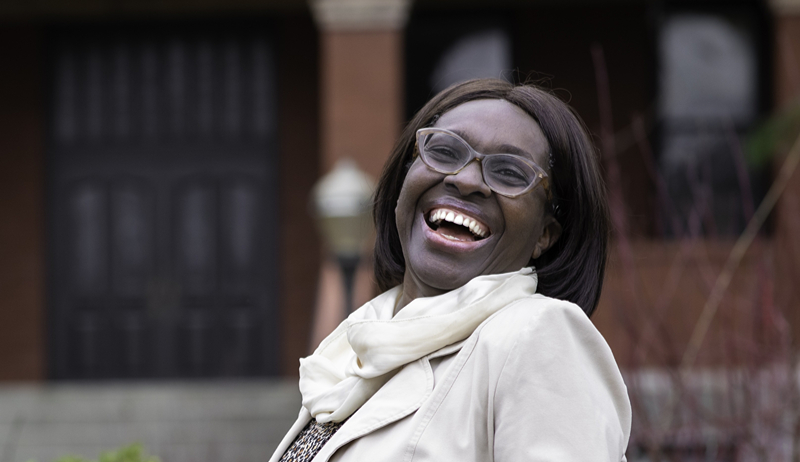 An image of Dean of CHEA Nyaradzo Mvududu smiling as she stands in front of Peterson Hall on the SPU campus.