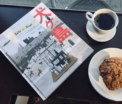 isle of the dogs book sits on table with coffee and muffin