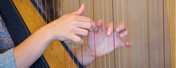 Closeup of the hands of a music therapy graduate playing the harp