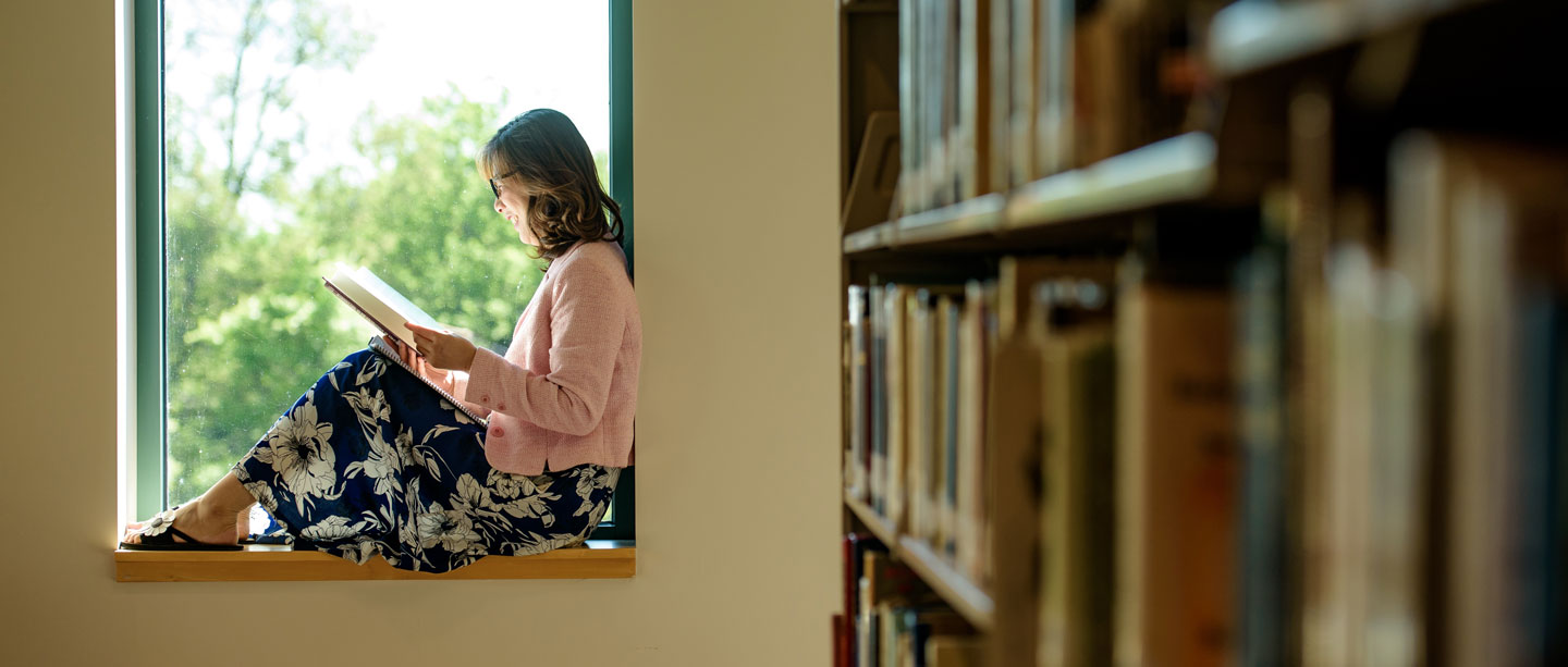 student reads a book next to window in library