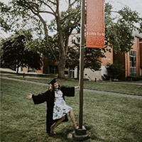 Anam Qadri, hanging off of a lamppost on campus in cap and gown
