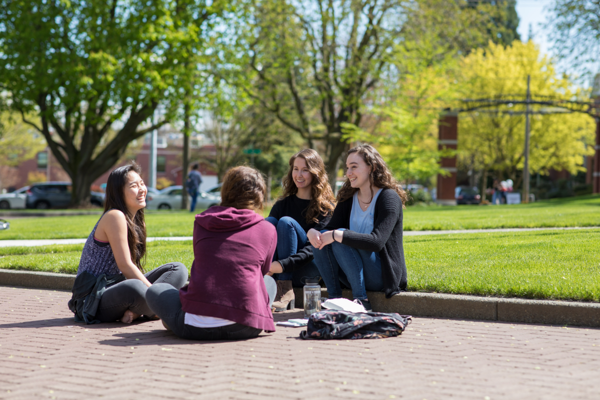 Four female SPU students sitting in Tiffany Loop, talking and laughing