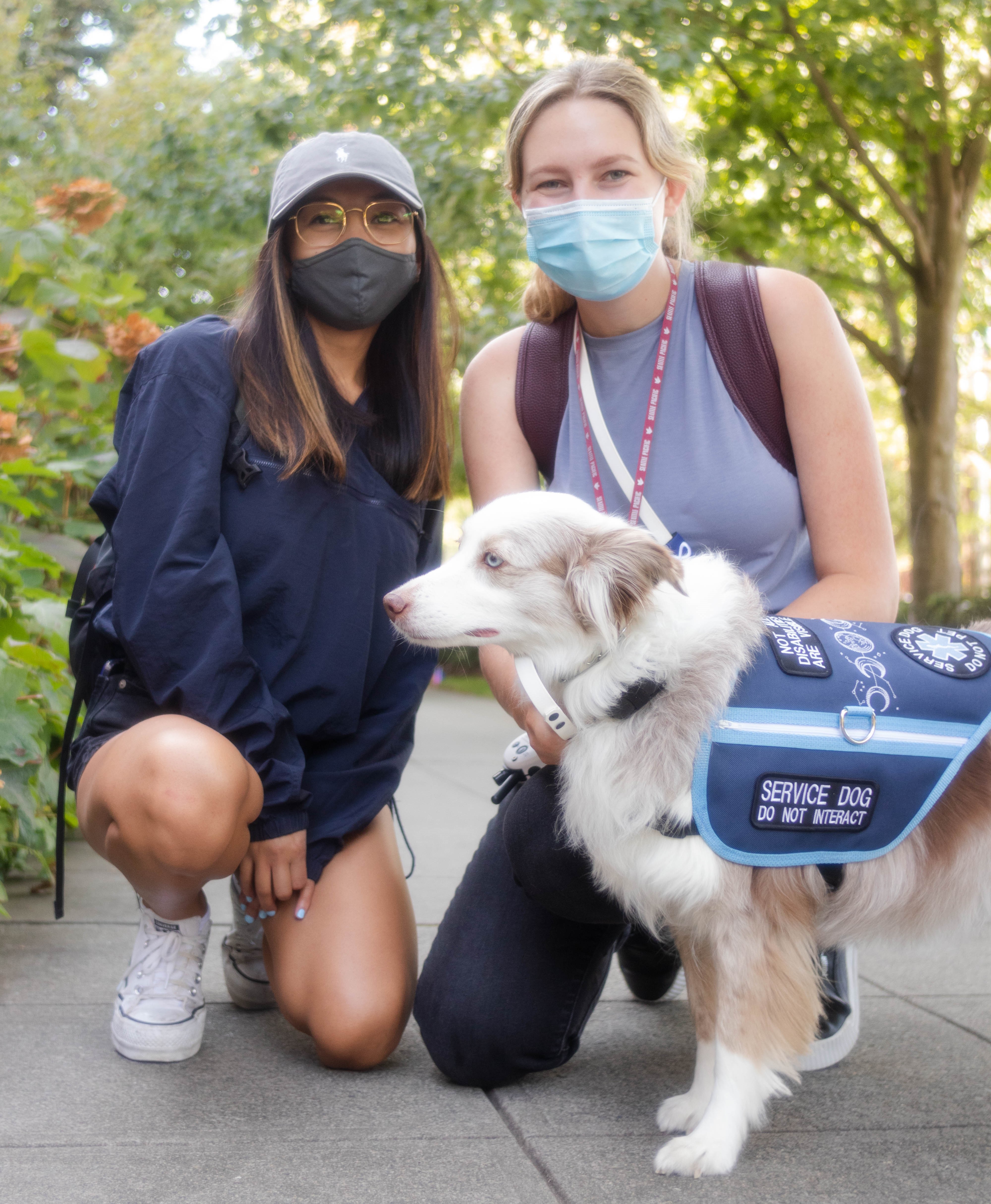 Two students crouch outside with a service dog.