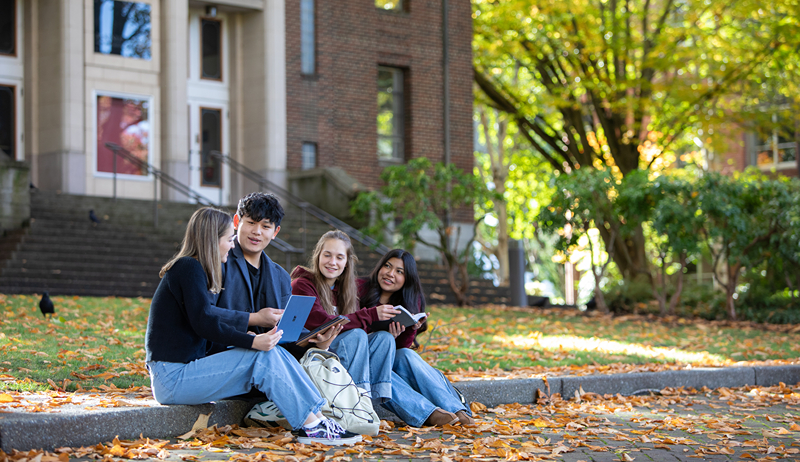 Four SPU students sitting on the curb in Tiffany Loop during the autumn.