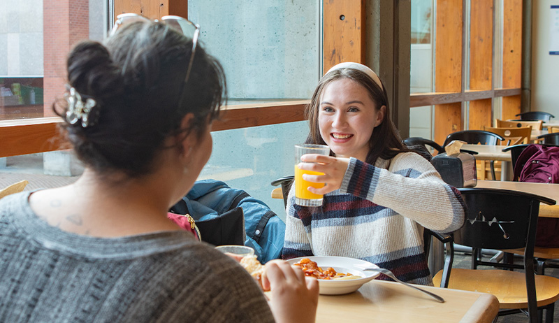 Two SPU students sit at a table next to the window while enjoying their meal in Gwinn Commons