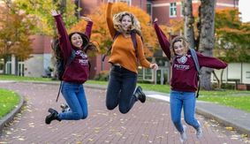 Three SPU student jump and laugh while in Tiffany Loop