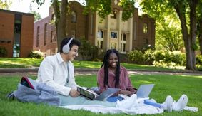 Two SPU students sit, laughing and talking, on blankets in Tiffany Loop.