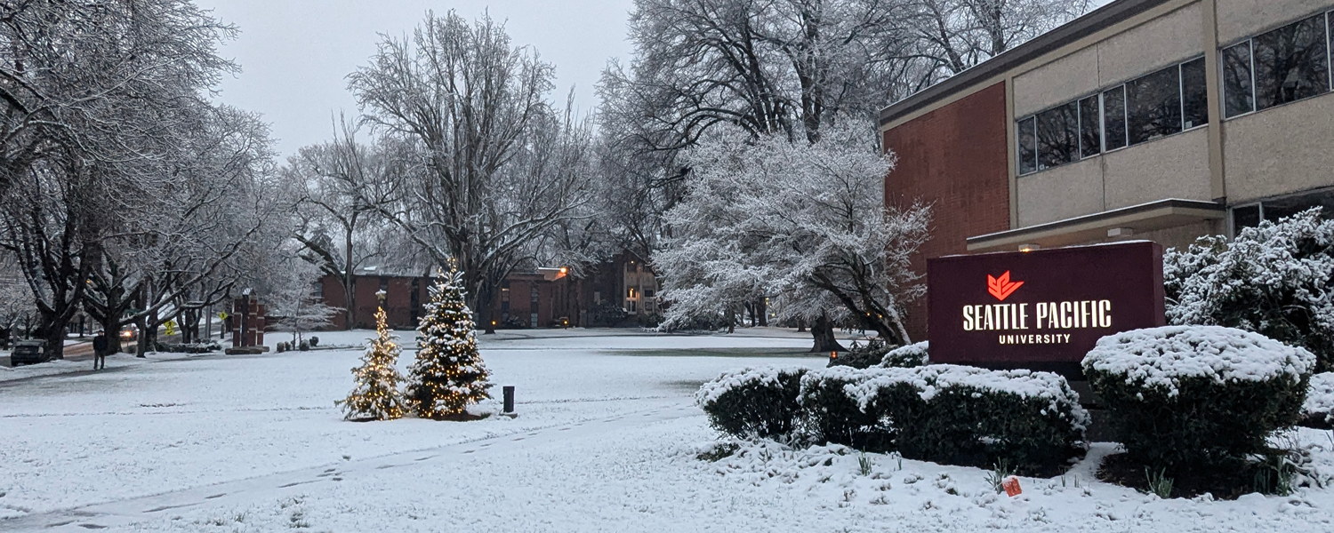Lower campus outside the Student Union Building on the Seattle Pacific University campus is blanketed with snow. Two lighted Christmas trees sit off to the side.
