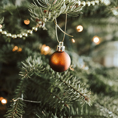 Close-up of an orange ball-shaped Christmas ornament, hanging on the branch of a tree
