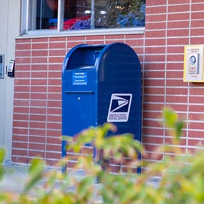 A large blue U.S mailbox sits near the wall outside the Student Union Building on the SPU campus