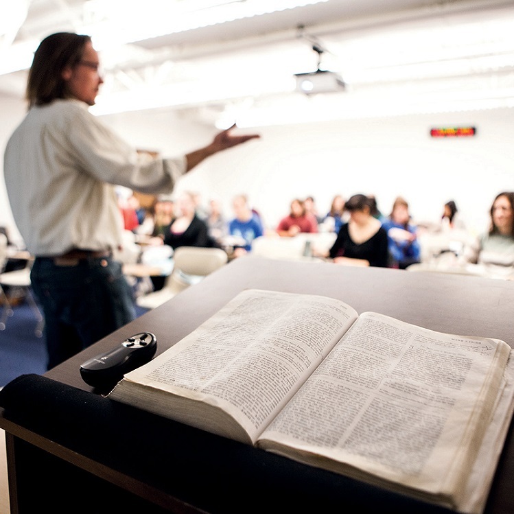 Professor of New Testament David Nienhuis talks to his SPU students. A Bible sits open on a lectern in the foreground.