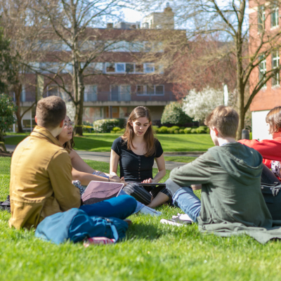 Four SPU students sit cross-legged on the grass in Tiffany Loop