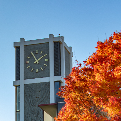 The Demarary Hall clock tower with the blue sky above it and colorful autumn leaves in front of it on the Seattle Pacific University campus