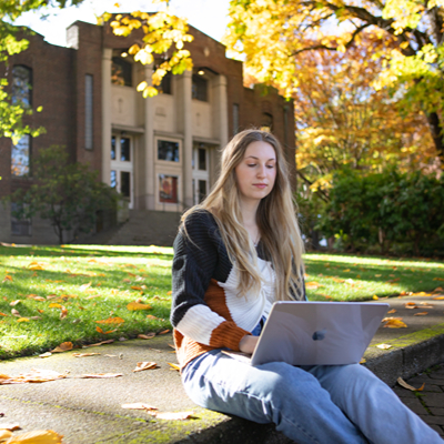 A female SPU students sits in Tiffany Loop with a laptop opened in her lap