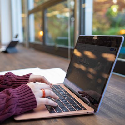 An SPU student with her fingers over her laptop as she sits at a table in the student lounge in Weter Hall.