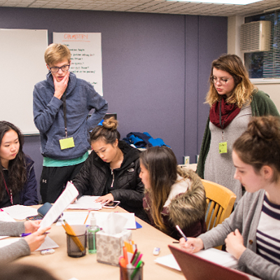 Two peer tutors, a male student and a female student, stand behind a table with other SPU students seated to work on their school work.