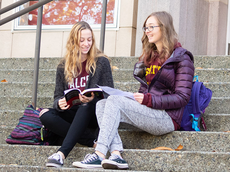 Two SPU students sit on the steps of the theater, talking