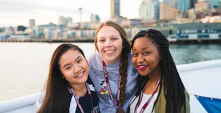 Three students smiling to camera with Seattle skyline in the background