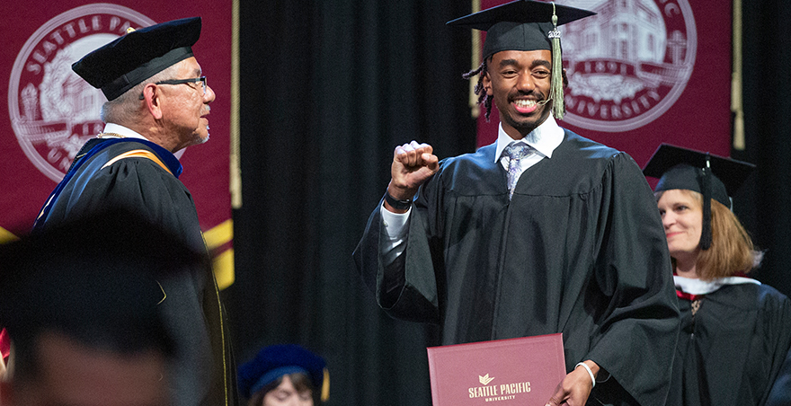 A student in his cap and gown excitedly cheering after receiving his SPU undergraduate diploma at Commencement