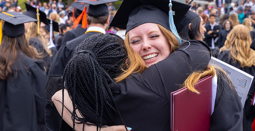 Students in their cap and gown hug after SPU