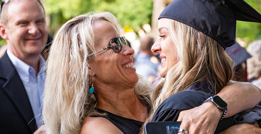 A mother hugs her daughter who is dressed in her cap and gown at SPU