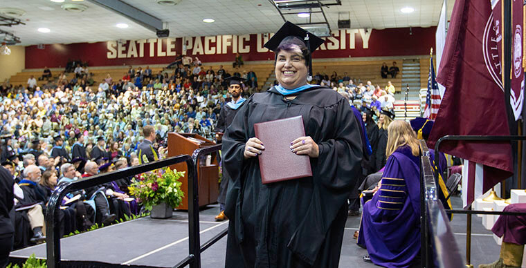An SPU graduate student walks across the stage during the 2019 Graduate Commencement ceremony - photo by Dan Sheehan