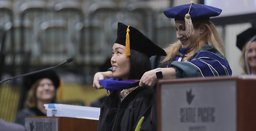 An SPU professor drapes a hood over the shoulders of a new master's degree recipient.