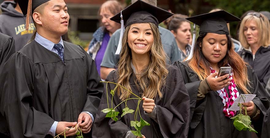 Three undergraduate graduates, wearing their caps and gowns in Tiffany Loop, celebrate after participating in Ivy Cutting.