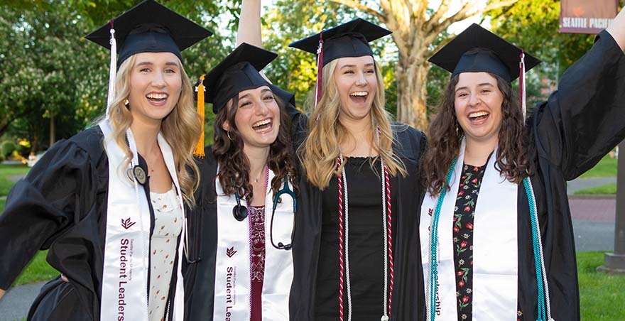 Four new graduates from Seattle Pacific University stand shoulder to shoulder as they celebrate their graduation from SPU.