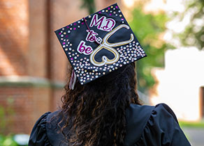 An SPU graduate with a decorated mortarboard reading "M.D. to be"