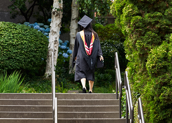 An SPU grad in cap and gown ascends a metaphorical and literal staircase | photo by Garland Cary